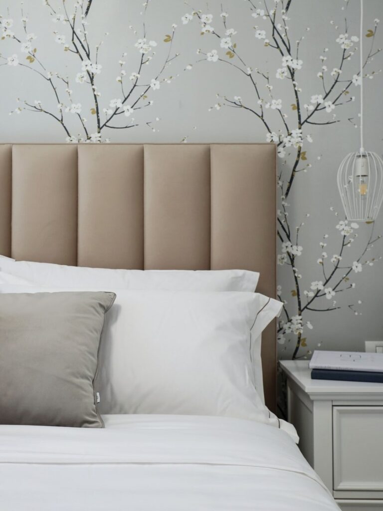 Dormitor amenajat care respecta regulile fengshui. In imagine putem vedea tablia unui pat, iar in spatele sau un tapet cu accente florale si o cromatica dechisa.