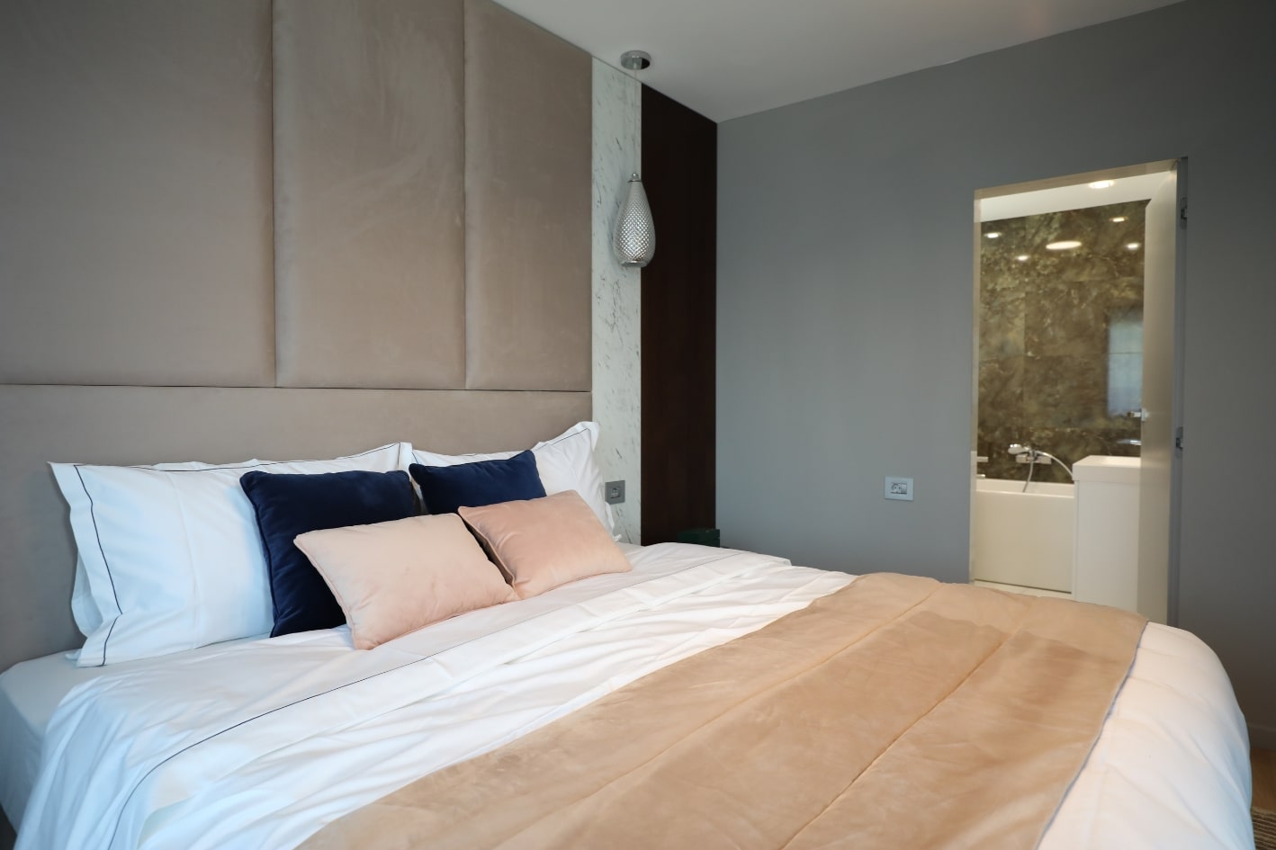 Design interior dormitor matrimonial inalt cu un pat mare si materiale textile de culoare alba si roz.